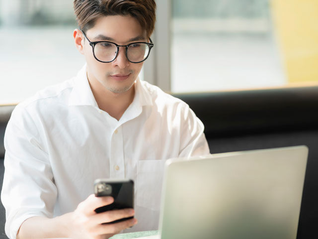 Joven de edad indeterminada consultando móvil y portátil