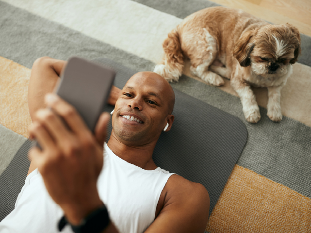 Un usuario tumbado en el suelo junto a su mascota mientras consulta el móvil