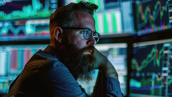 Hombre consultando varios monitores con información financiera