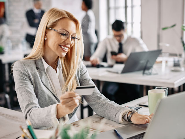 Usuaria con una tarjeta de crédito en una mano consultado el portátil